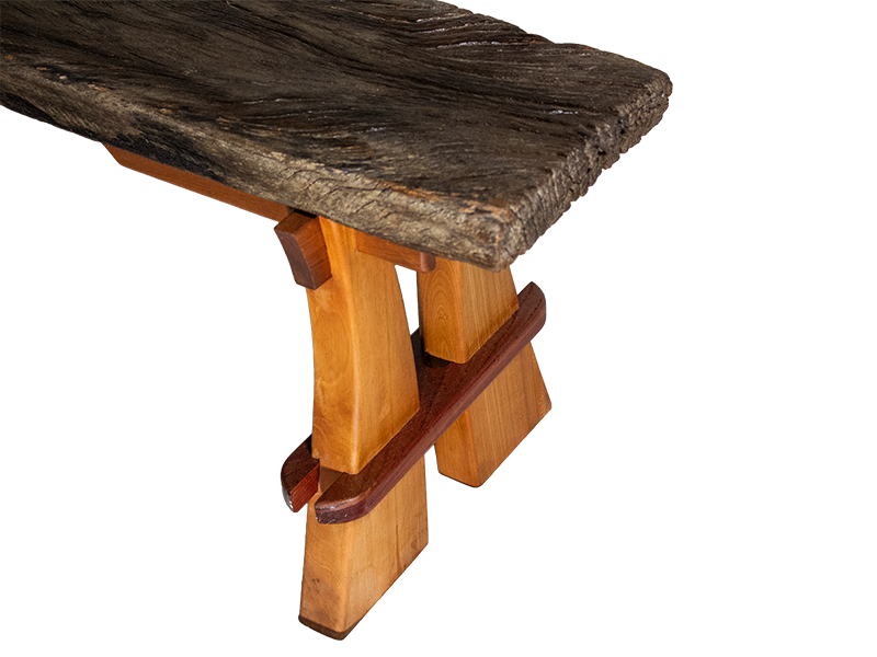 Weathered mahogany waterfall bench with sculpted split leg and purple heart accents. Upper end of board view.