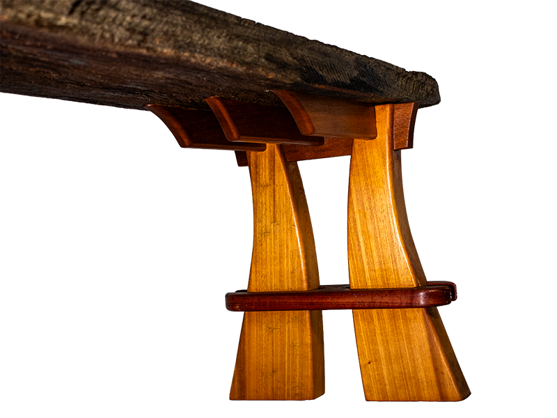 Weathered mahogany waterfall bench with sculpted split leg and purple heart accents.  Underside angle.